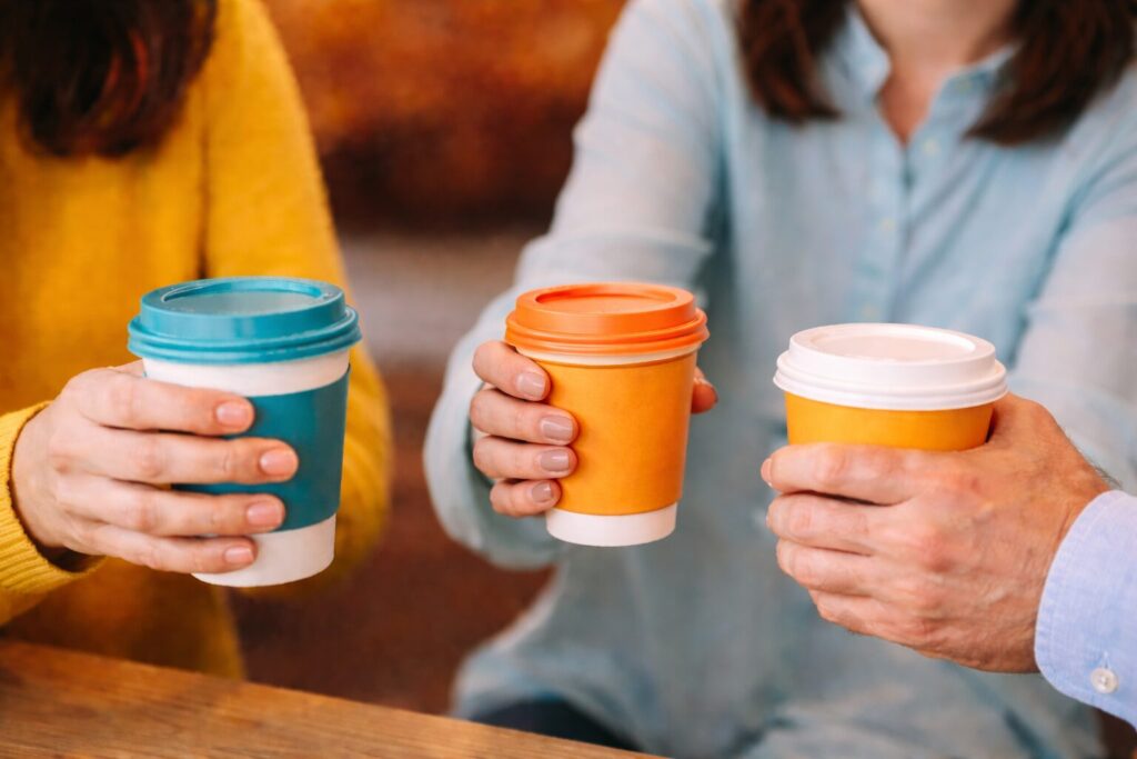 Plusieurs personnes se réunissent autour de tasses de café tenues dans les mains, symbole de rencontre conviviale et d’échanges entre participants.